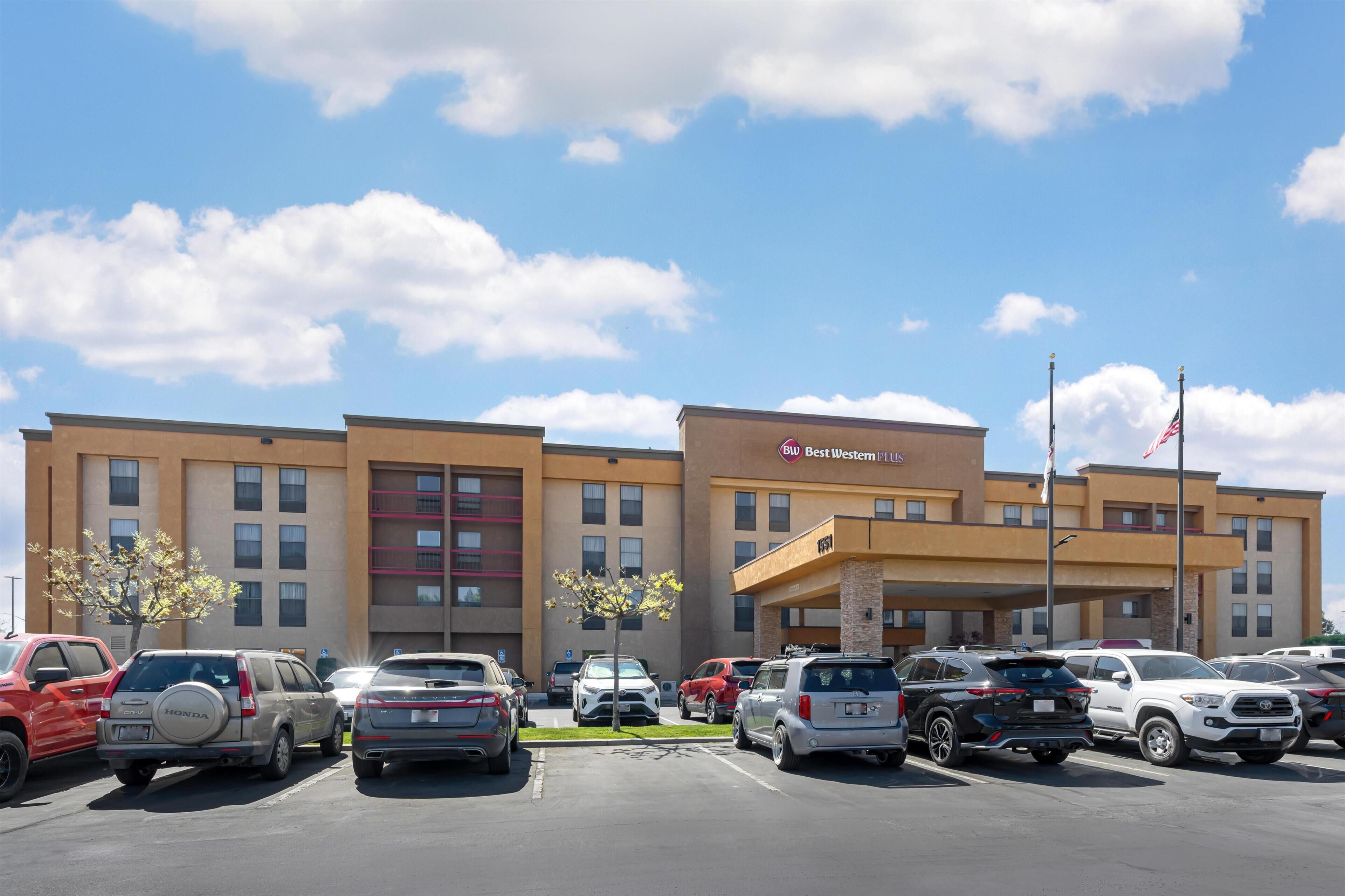 A hotel with a parking lot, multiple cars, and a clear sky.