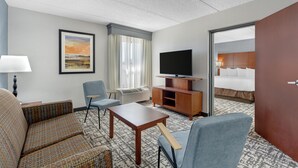 Une chambre d’hôtel avec un canapé, un fauteuil, une télévision et un lit.