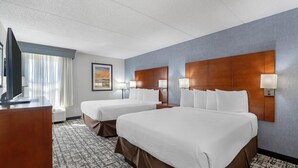 Une chambre d’hôtel avec deux lits, un bureau, une télévision et une fenêtre avec des rideaux.