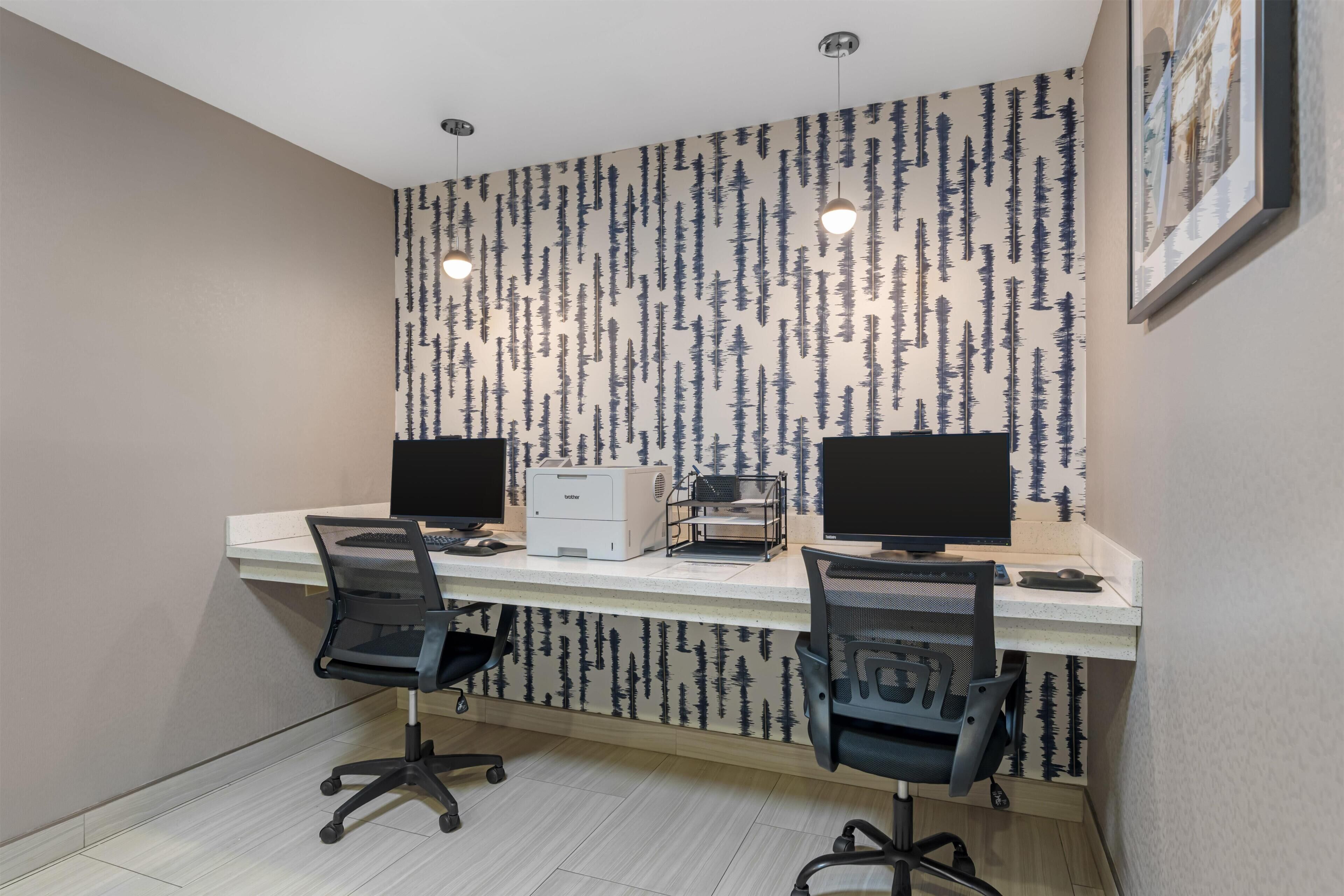A modern office with two desks, two chairs, a printer, and a wall with a vertical pattern.