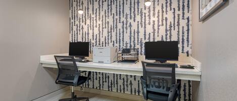 A modern office with two desks, two chairs, a printer, and a wall with a vertical pattern.