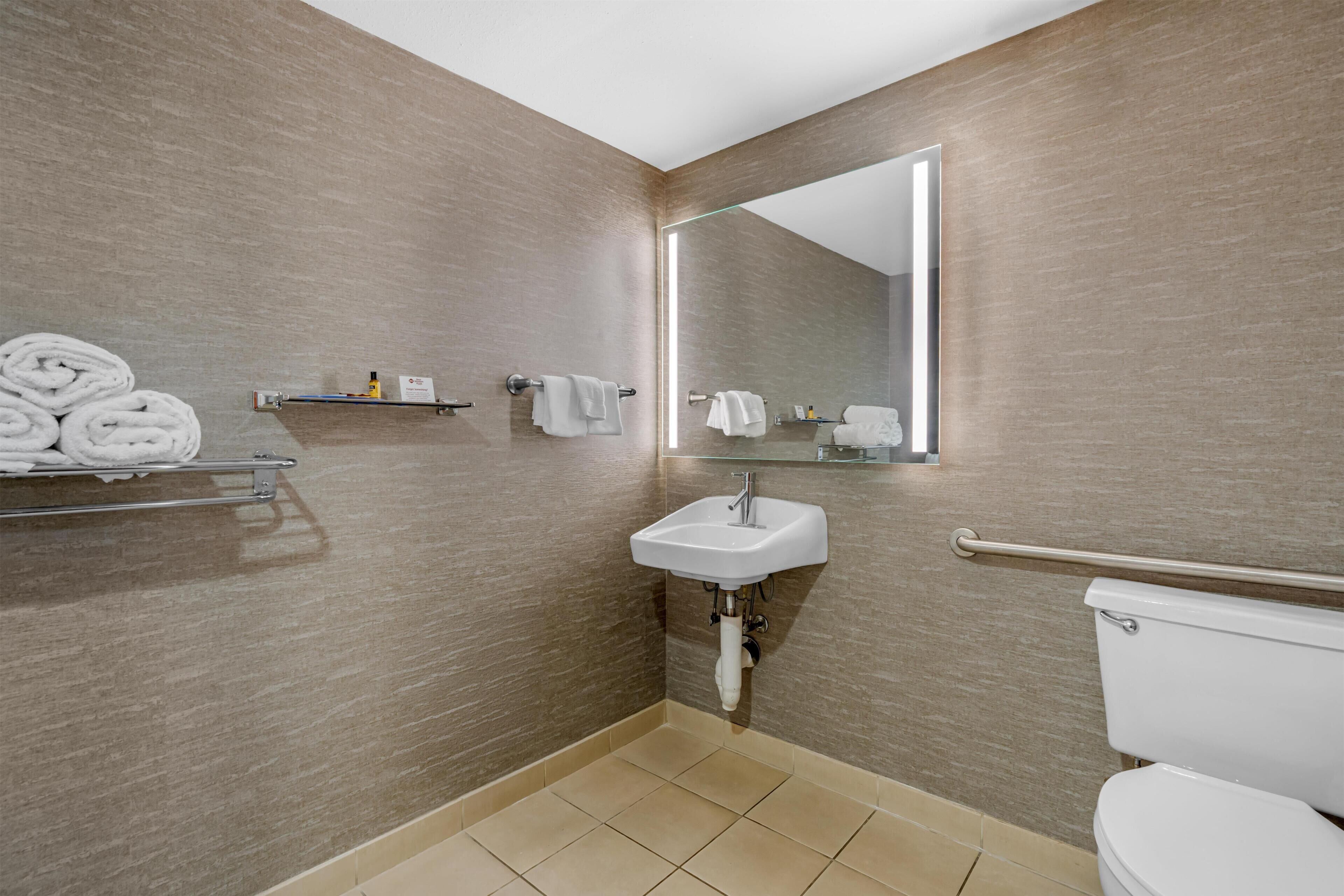 Un baño con lavamanos, espejo, toallero y retrete.