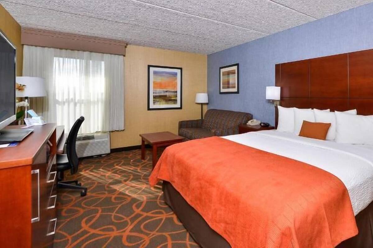 Une chambre d’hôtel avec un lit, un bureau, une chaise et deux tableaux accrochés au mur.