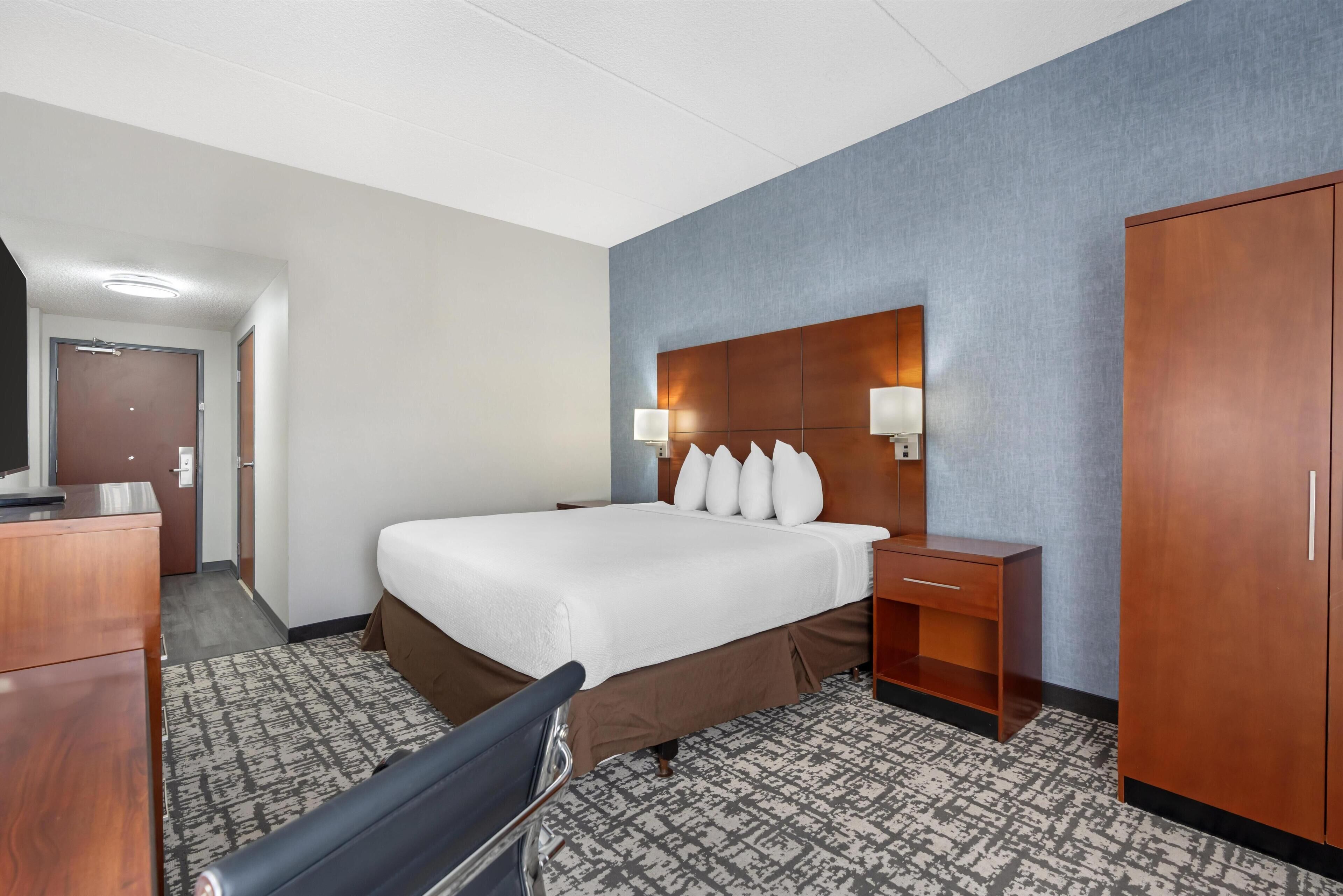 A hotel room with a large bed, a desk, a wardrobe, and a television.