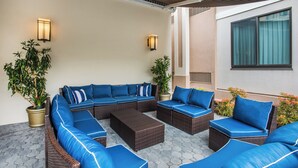 Un espace extérieur aménagé, abrité et doté de mobilier en osier et de coussins bleus, de plantes en pot et d’un éclairage fixé au mur.