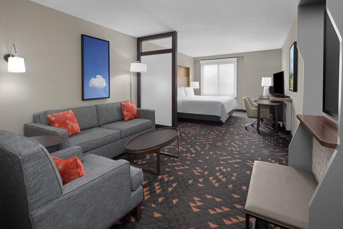 Une chambre d’hôtel avec un canapé gris, une petite table ronde, un lit, un bureau avec une chaise et un téléviseur.
