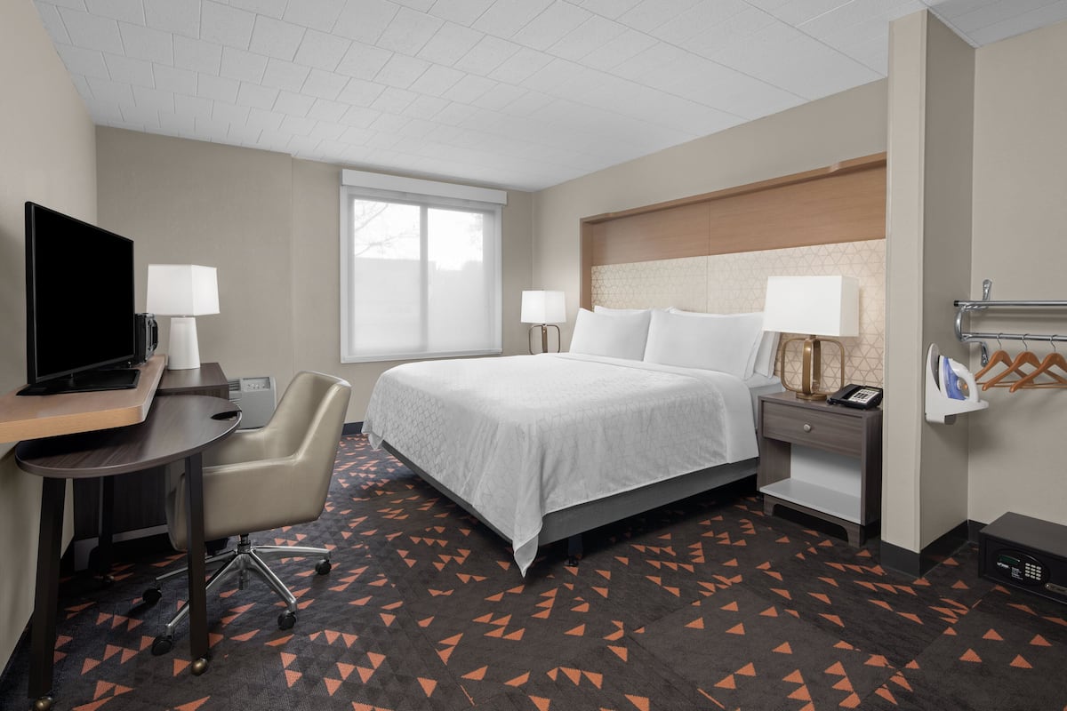 Habitación de hotel con cama, escritorio, silla, televisor, lámparas de noche y ventana.