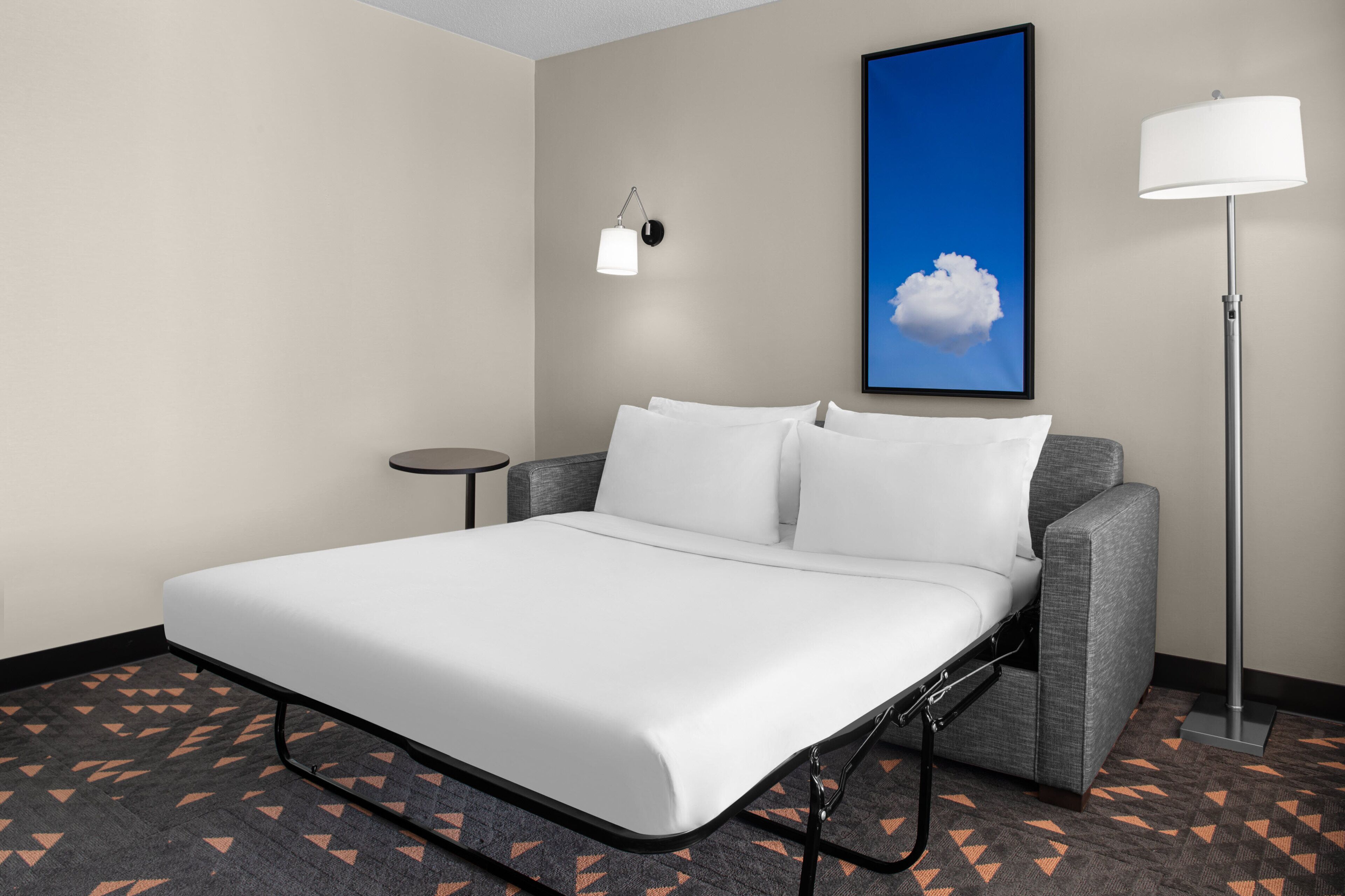 A hotel room with a bed, a side table, a lamp, and a framed picture on the wall.