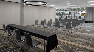 A conference room with a long table and multiple chairs, carpeted floor with a geometric pattern, and a large circular light fixture.