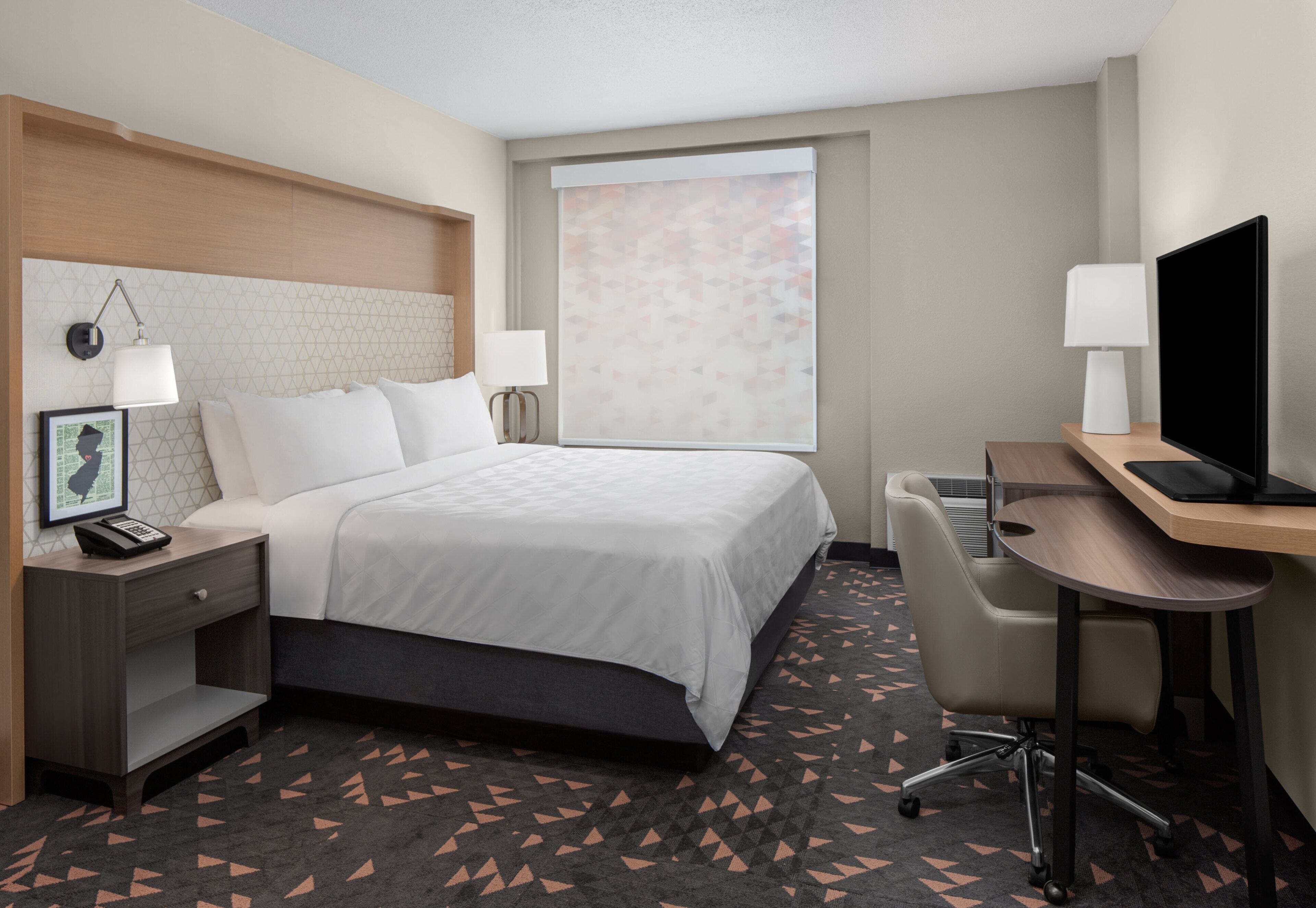 A hotel room with a bed, bedside tables, a desk with a chair, a television, and a window with a view.