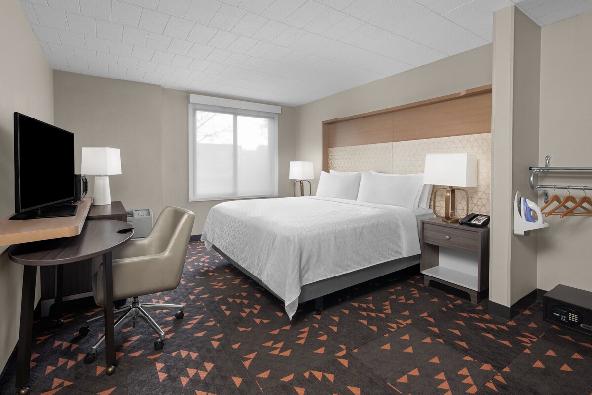 Une chambre d’hôtel équipée d’un lit, d’un bureau, d’une chaise, d’une télévision, de lampes de chevet et d’une fenêtre.