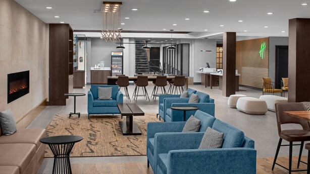 Un hall d’hôtel moderne avec des canapés bleus, une cheminée, un coin bar et une cuisine en arrière-plan.