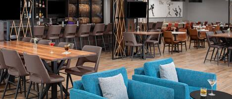 A modern restaurant with wooden tables and chairs, blue sofas, and a bar area with barrels.