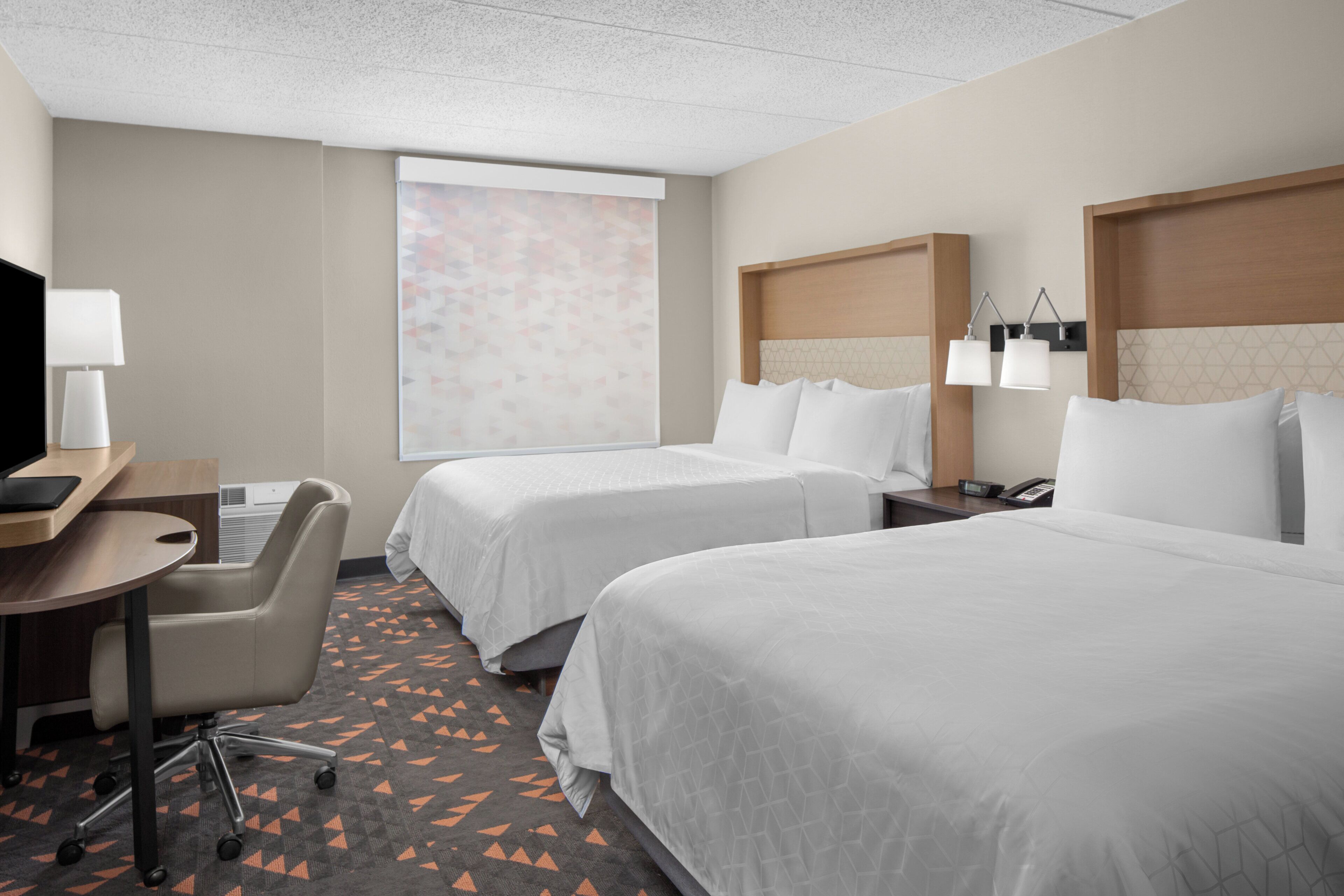 Une chambre d’hôtel avec deux lits, un bureau, une chaise, une télévision et une fenêtre donnant sur un paysage agréable.