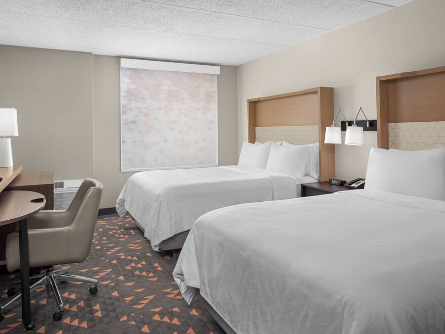 Une chambre d’hôtel avec deux lits, un bureau, une chaise, une télévision et une fenêtre donnant sur un paysage agréable.