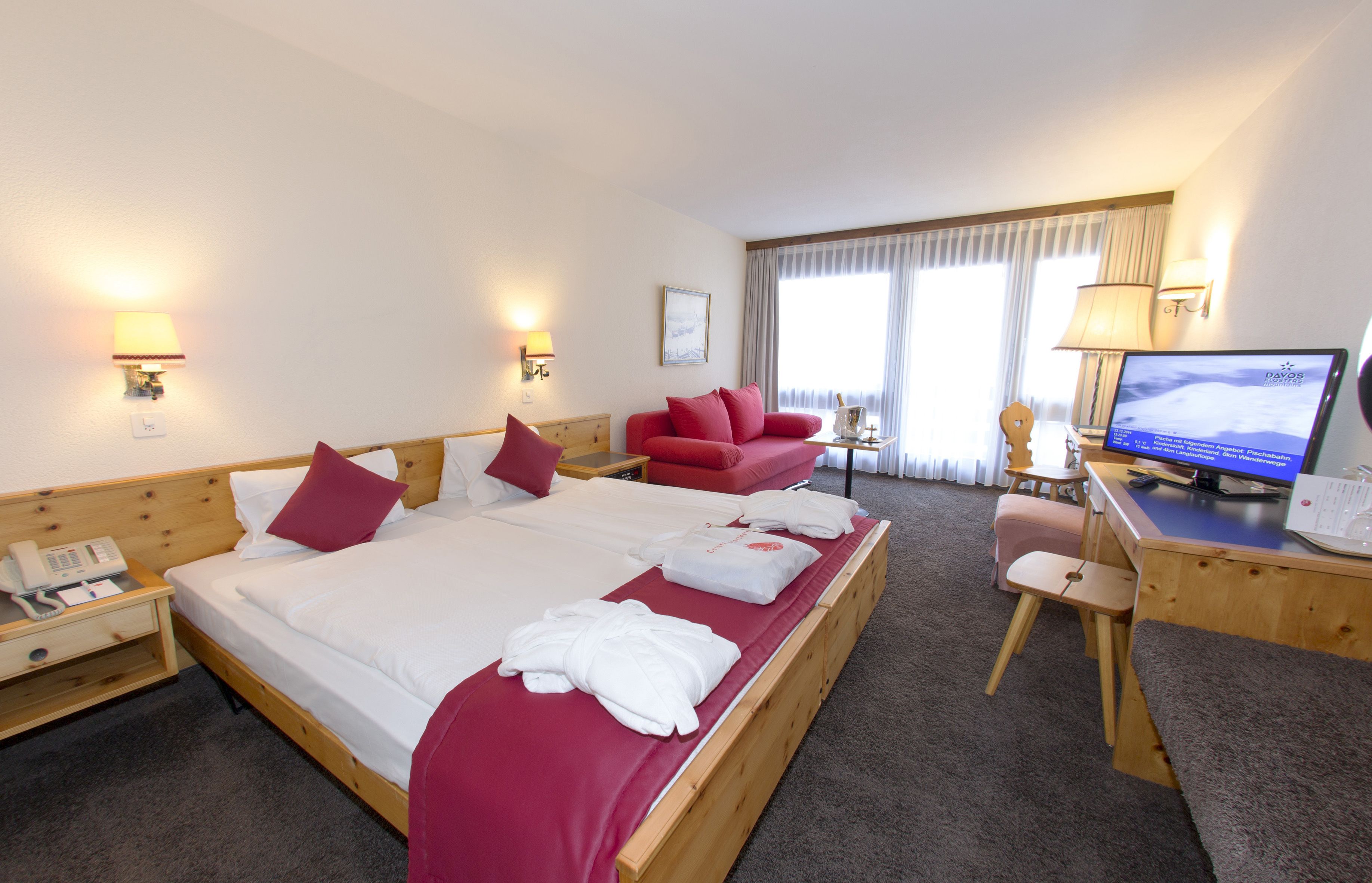 A hotel room with a large bed, a desk with a computer, a chair, and a small table.