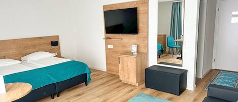 Une chambre d’hôtel moderne équipée d’un lit, d’un bureau, d’une télévision, d’un miroir et d’un coin salon.