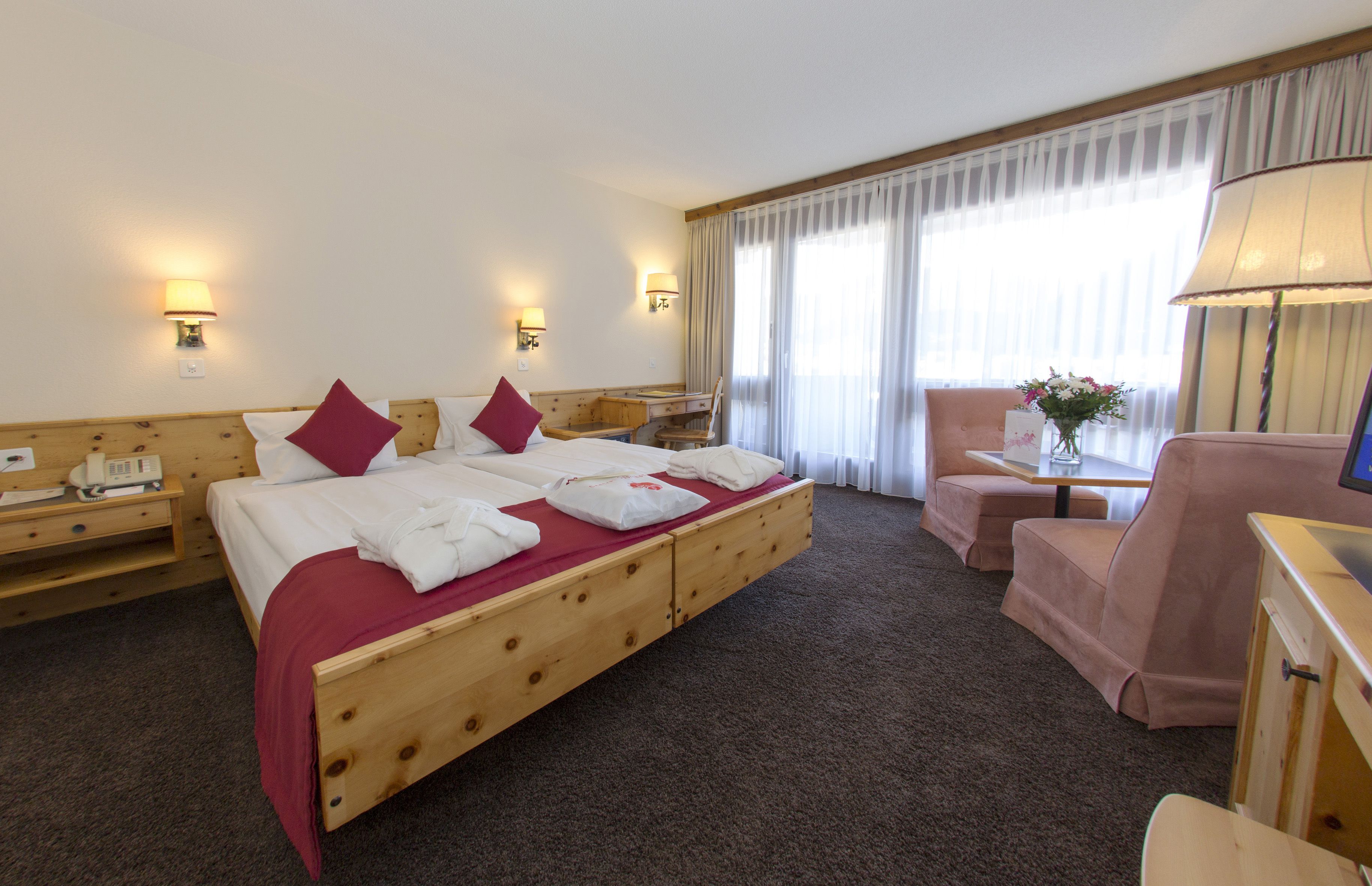 A hotel room with a wooden bed, a desk, a chair, and a television.