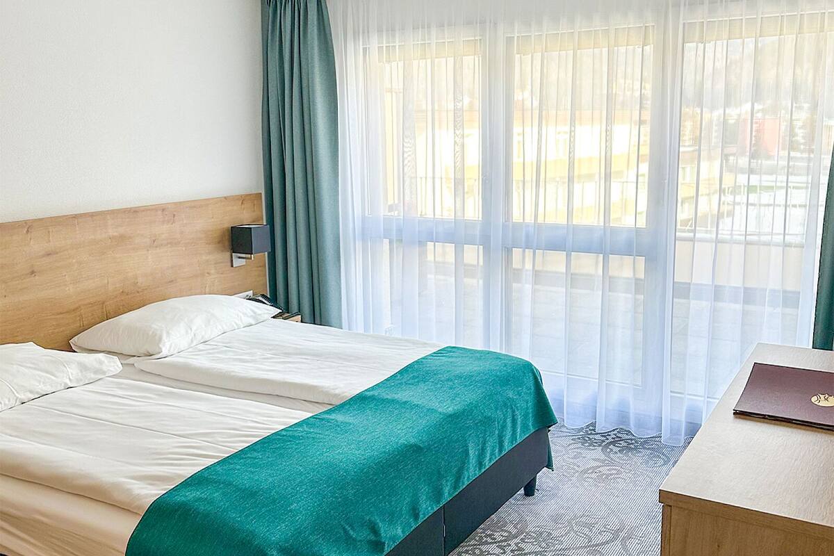 A hotel room with a bed, a desk, and a window with curtains.