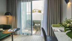 Habitación de hotel con sofá verde, una mesita redonda pequeña, una mesa de comedor con sillas, una lámpara y vistas a través de una puerta de vidrio.