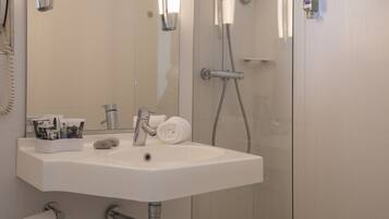 A bathroom with a white sink, a mirror, a shower with a glass door, and a toilet.