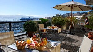 Una terraza con una mesa dispuesta para el desayuno, un ordenador portátil y vistas al puerto deportivo y al paisaje urbano.