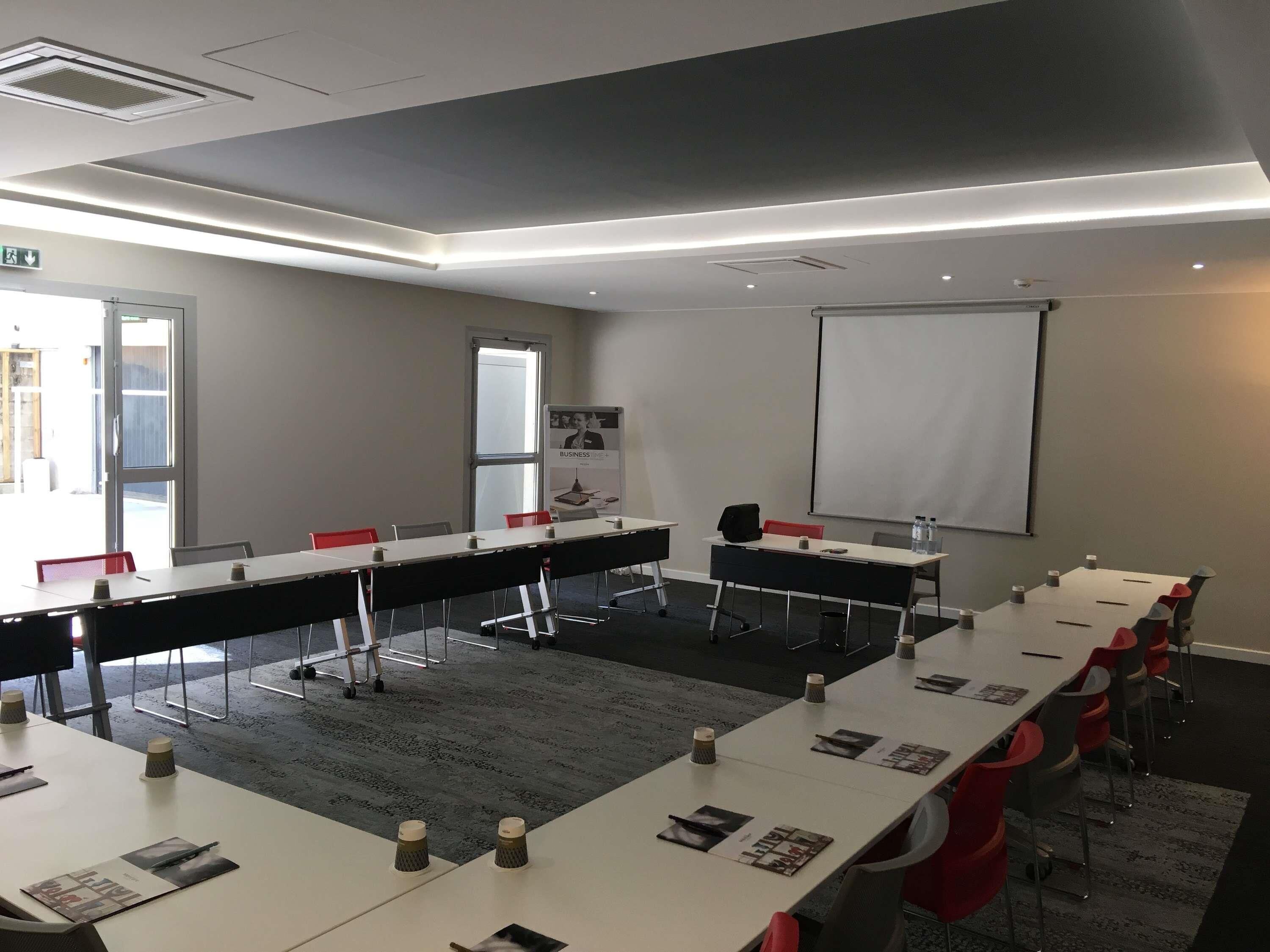 Une salle de conférence équipée de longues tables, de chaises et d’un écran de projection.