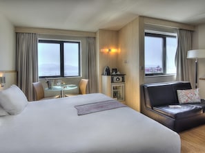 Et hotelværelse med en stor seng, et spiseområde, en sofa, et minibar og havudsigt.