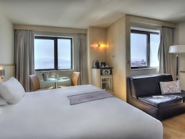 Habitación de hotel con una cama grande, zona de comedor, sofá, minibar y vista al mar.