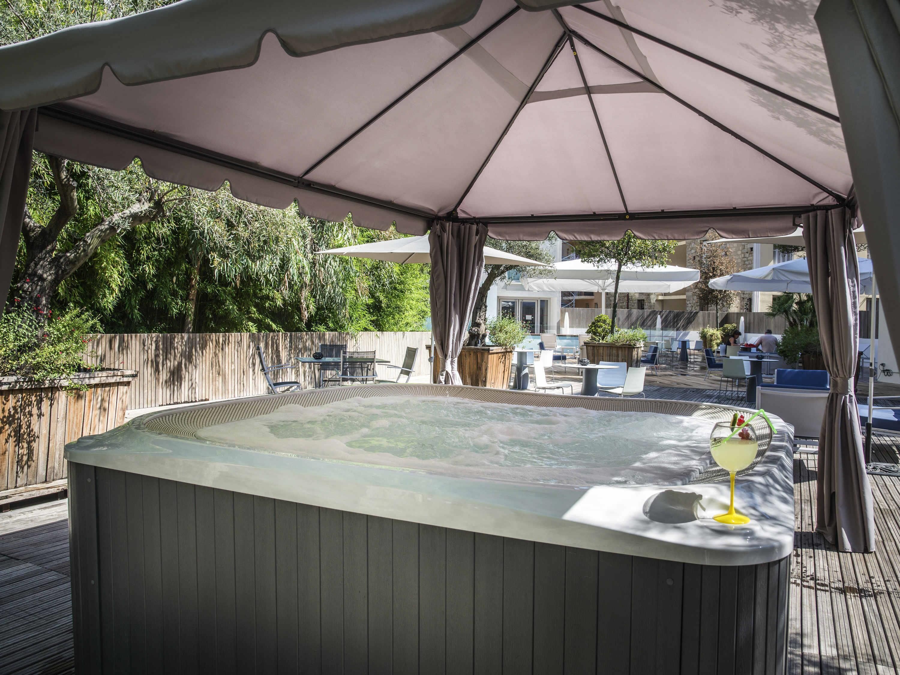 A hot tub with a table and chairs, surrounded by umbrellas and a wooden deck.