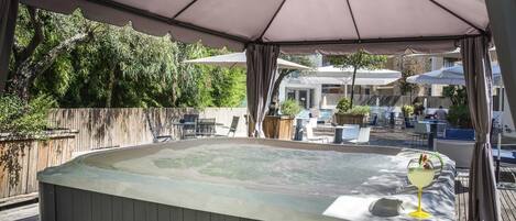 A hot tub with a table and chairs, surrounded by umbrellas and a wooden deck.