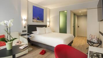 A modern hotel room with a large bed, a desk, a red chair, and a potted plant.