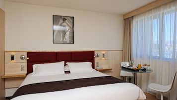 Habitación de hotel con una cama grande, una mesita de noche con lámpara, una pequeña mesa con artículos de desayuno y una silla.