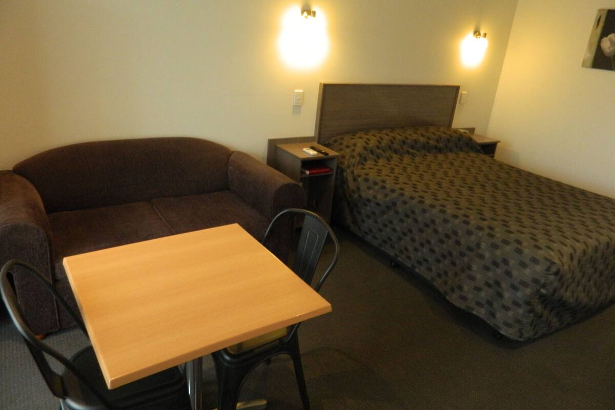 A compact room with a single bed, a sofa, and a small table.