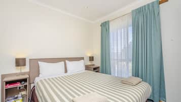 A hotel room with a large bed, two bedside tables, a nightstand, a lamp, and a window with curtains.
