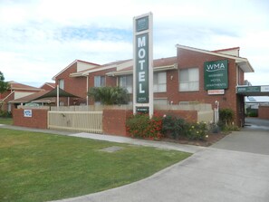 A motel with a prominent sign, brick buildings, and a fenced parking area. - Werribee Motel & Apartments (Werribee)