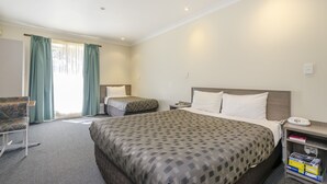 A hotel room with a large bed, two smaller beds, a desk with a telephone, a chair, and a bookshelf. - Werribee Motel & Apartments (Werribee)
