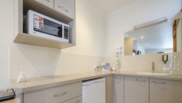 A modern kitchen with a microwave, dishwasher, and a large mirror above the sink. - Werribee Motel & Apartments (Werribee)
