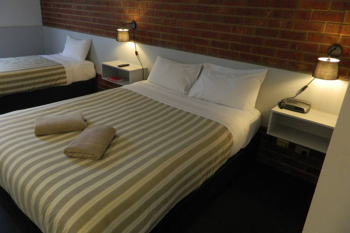 A hotel room with two beds, each with striped bedding and pillows, a brick wall, and bedside lamps.