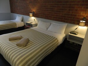 A hotel room with two beds, each with striped bedding and pillows, a brick wall, and bedside lamps. - Werribee Motel & Apartments (Werribee)