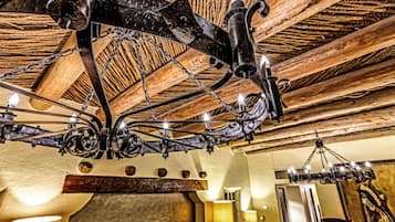 Un interior rústico con vigas de madera a la vista, un candelabro de hierro forjado y una chimenea de piedra.