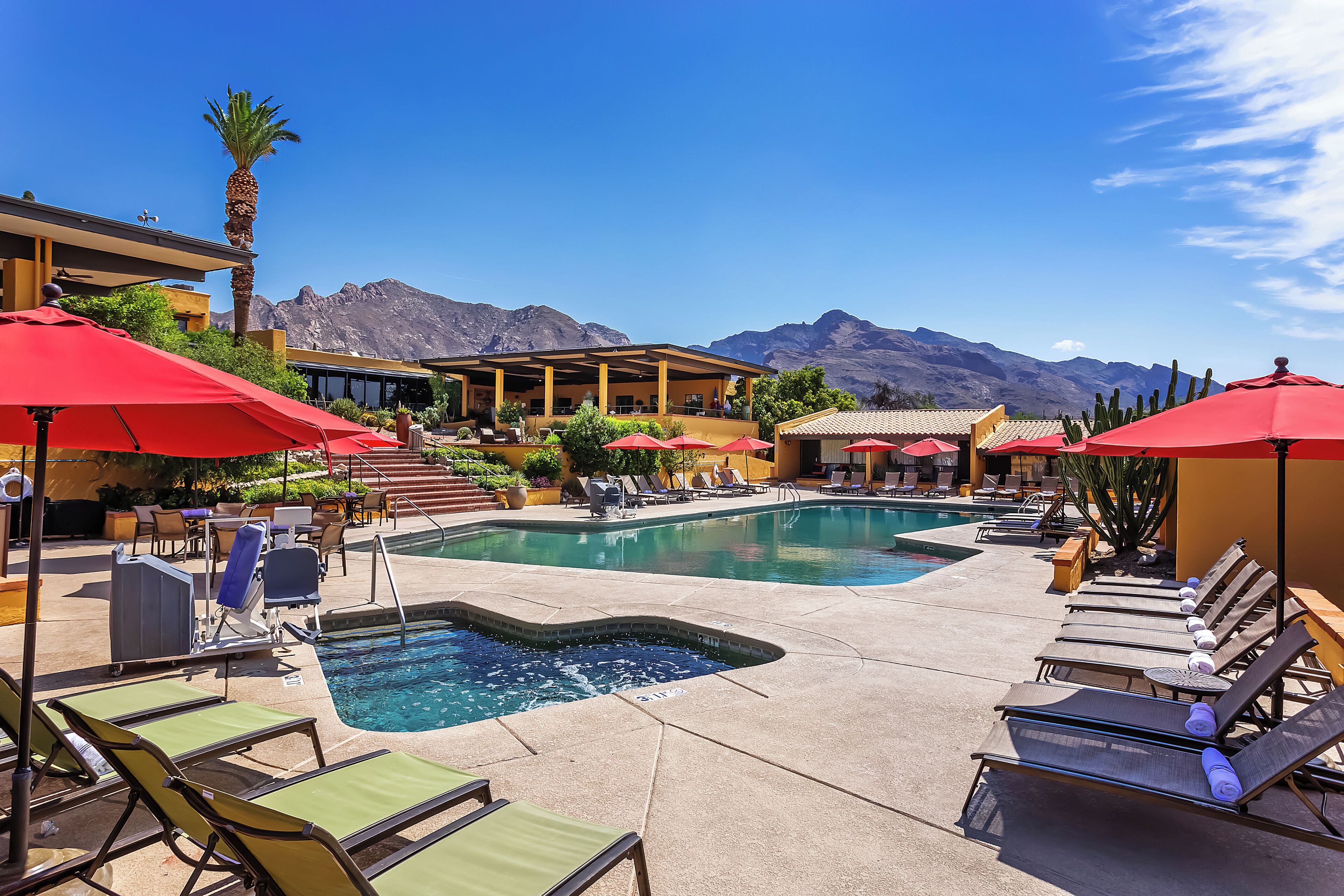 A pool area with lounge chairs and umbrellas, a pool, and mountains in the background.