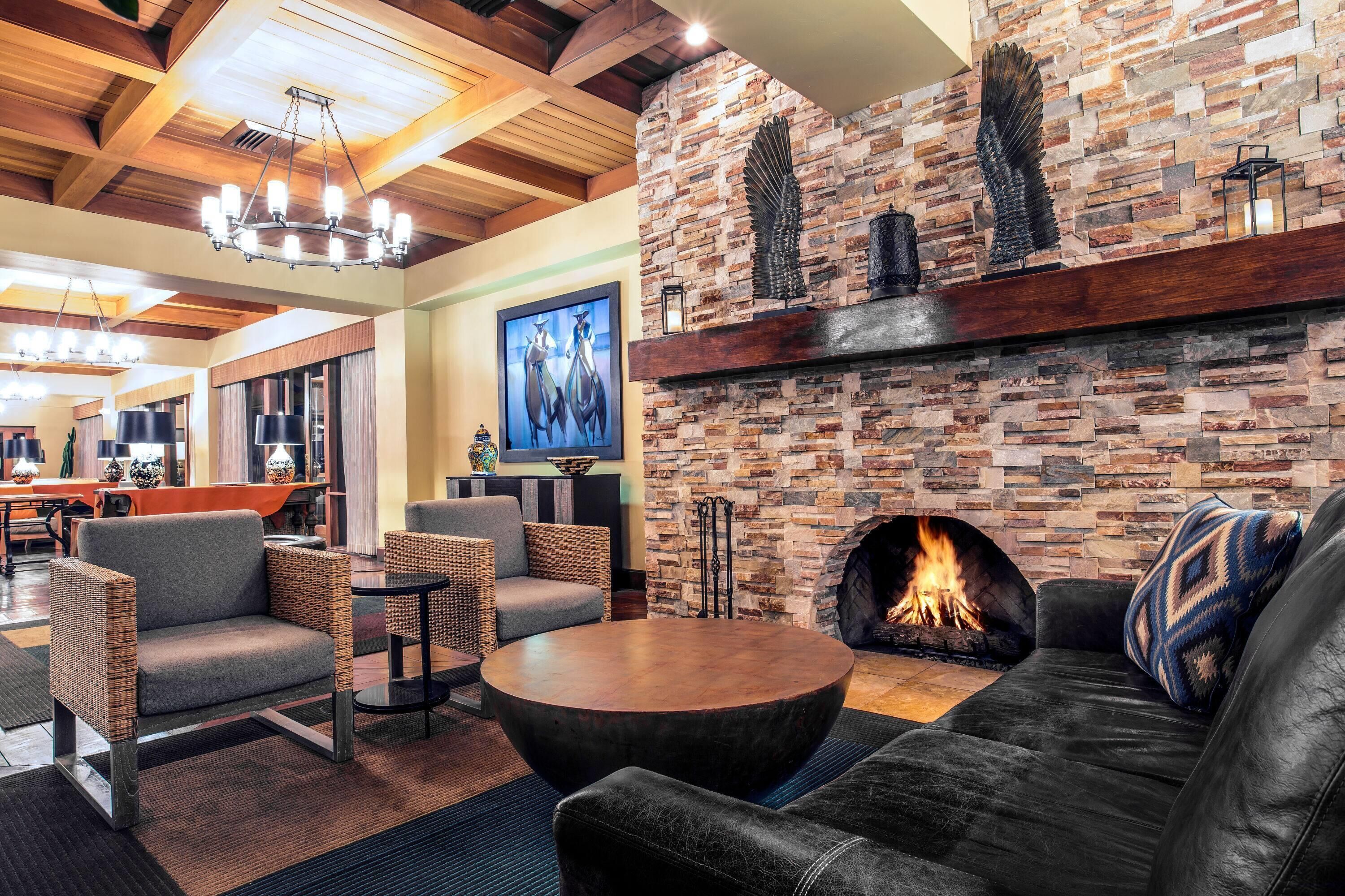 A cozy lounge area with a stone fireplace, comfortable seating, and a modern chandelier.