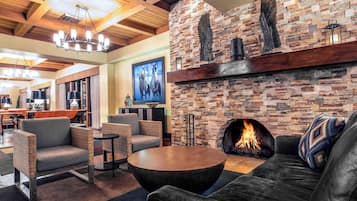 A cozy lounge area with a stone fireplace, comfortable seating, and a modern chandelier.
