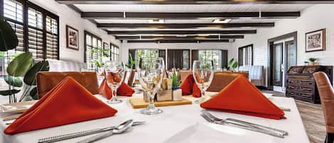 A dining area with a white table set for two, featuring red napkins and clear glassware.