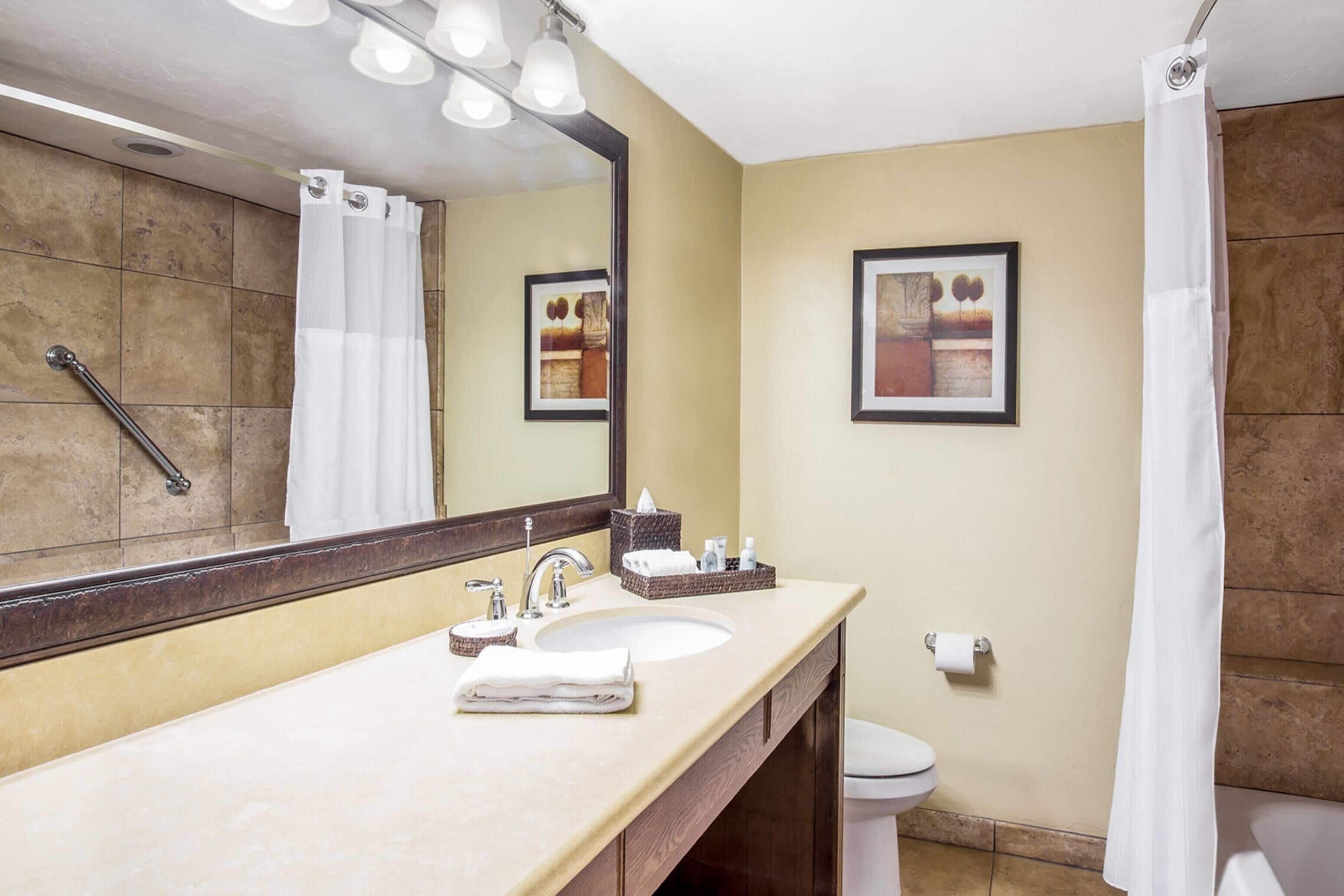 Une salle de bain équipée d’un lavabo, d’un miroir, de toilettes et d’un rideau de douche.