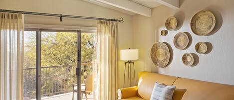 A living room with a sofa, a coffee table with magazines, a floor lamp, and a view of trees through a sliding door.
