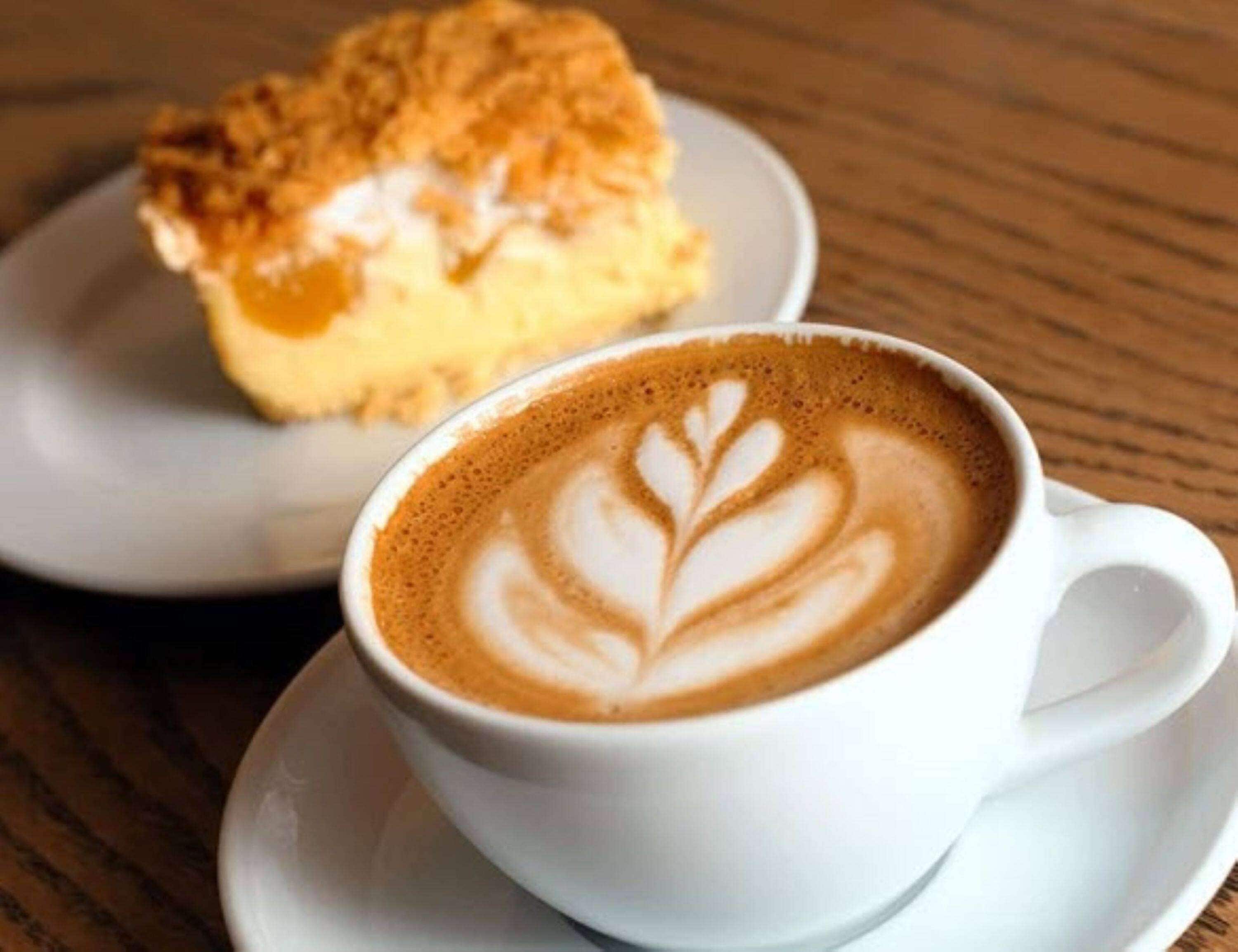Eine Tasse Kaffee mit Latte-Art auf einem Untertasse, platziert auf einem Holztisch.