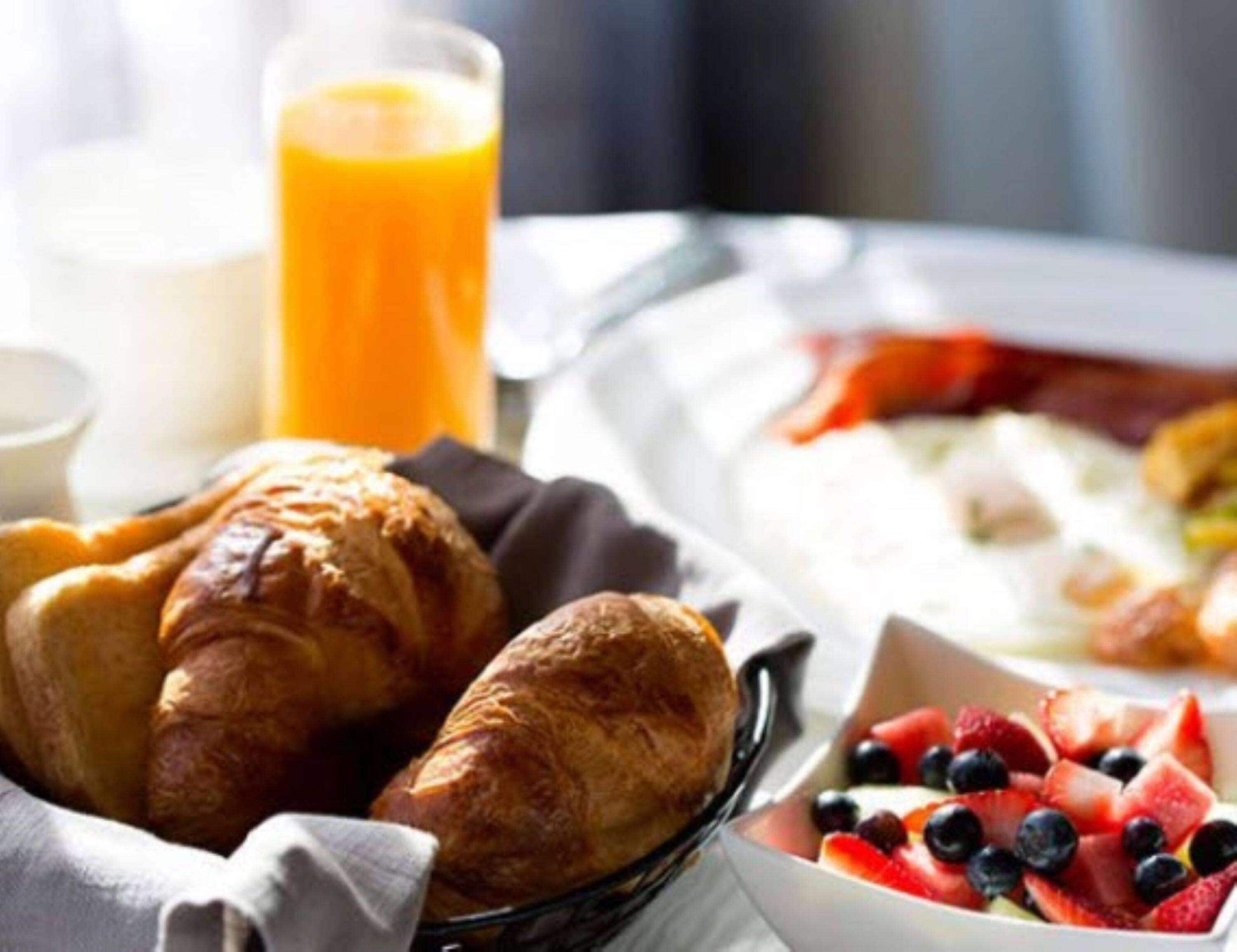 Un desayuno con cruasanes, un vaso de jugo de naranja, una fuente de fruta y huevos revueltos.