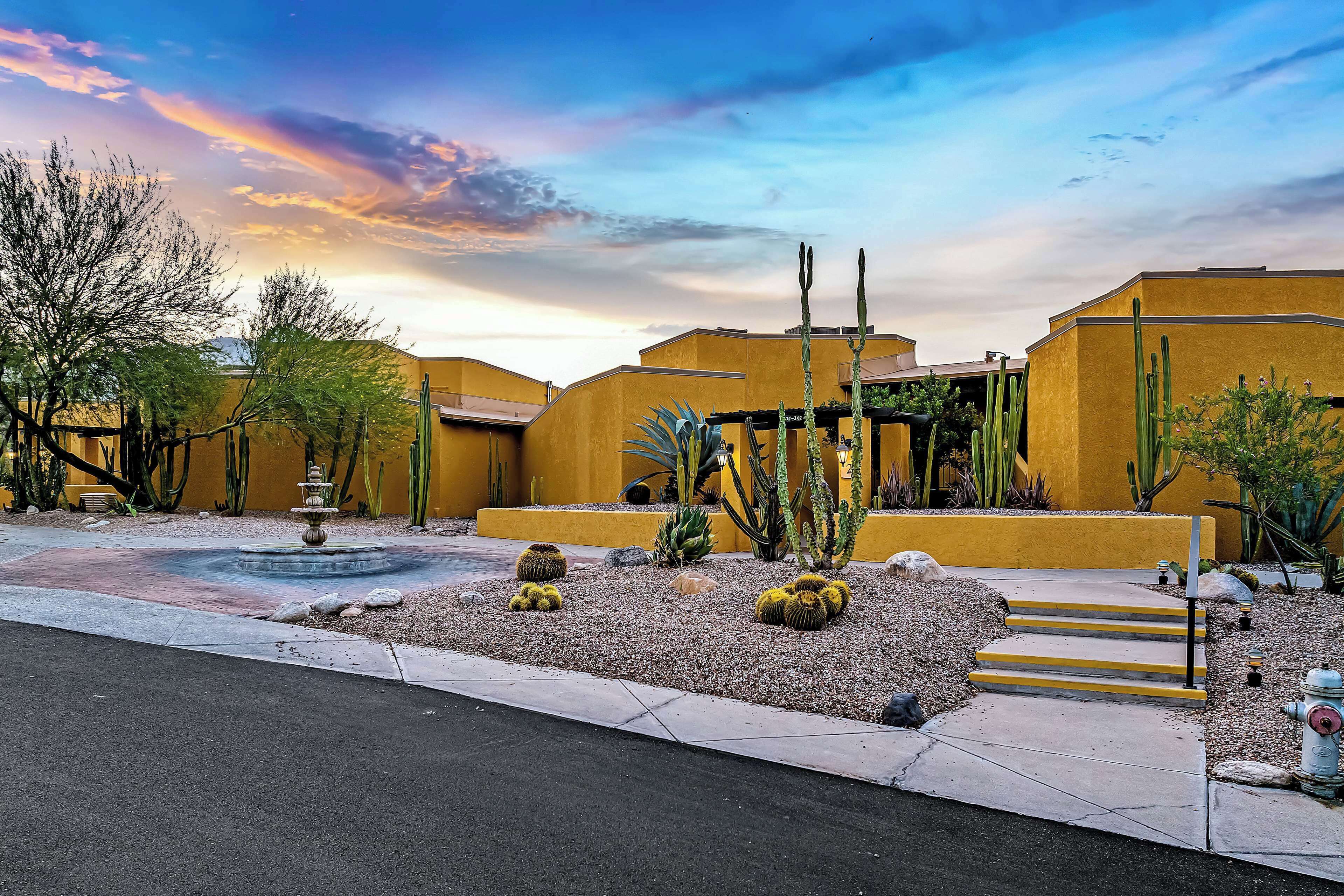 A courtyard with a fountain, cacti, and a building with yellow walls.